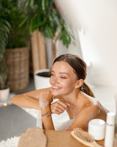 joyful-young-woman-smiling-away-and-leaning-on-bathtub-side-while-bathing-at-spa-resort.jpg